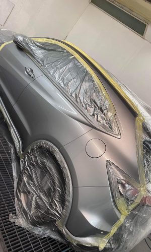 A car in the spray booth at highfeild coachworks there is plastic masking off the windows and lights and the whole left side has been painted silver