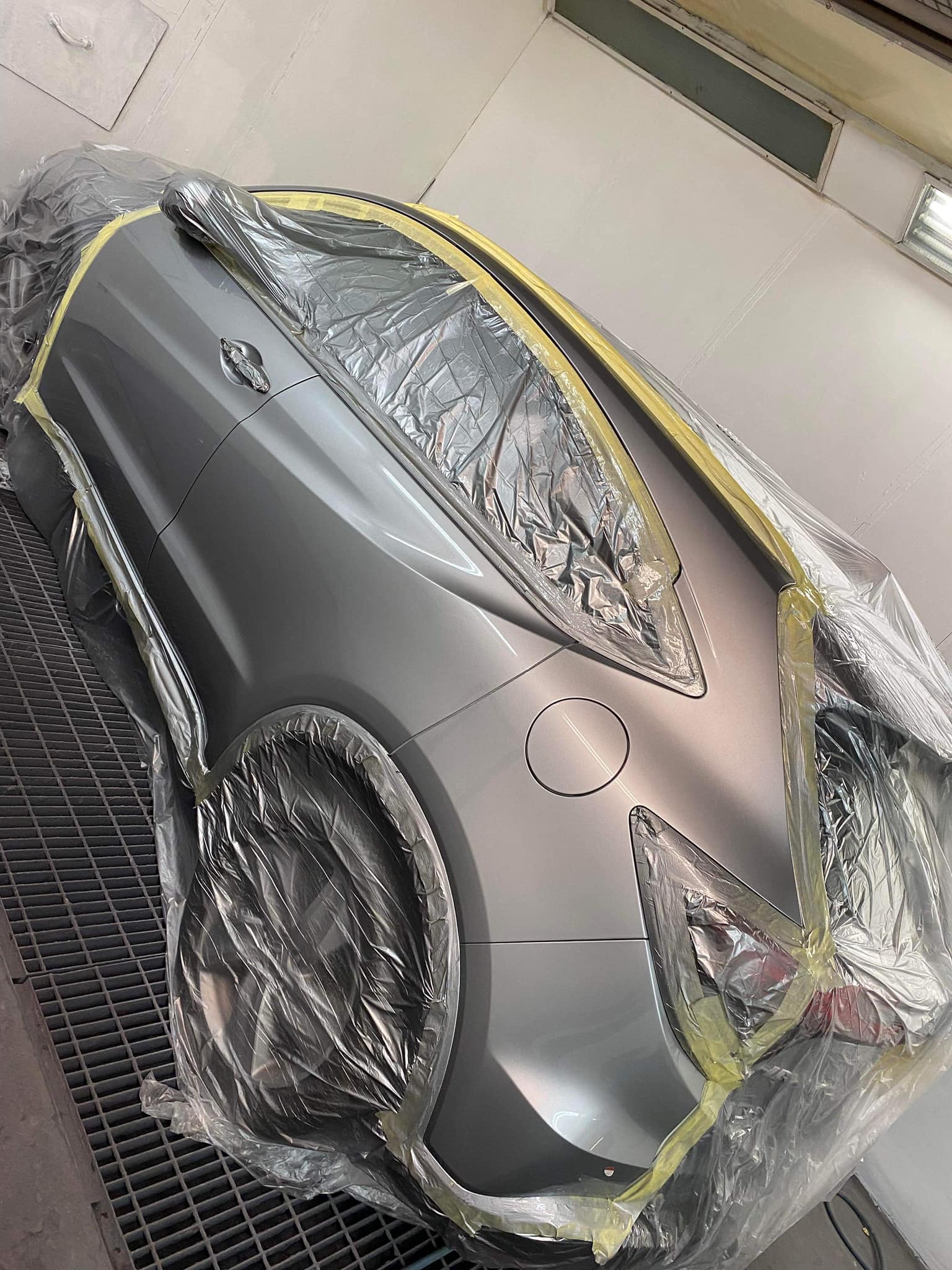A car in the spray booth at highfeild coachworks there is plastic masking off the windows and lights and the whole left side has been painted silver